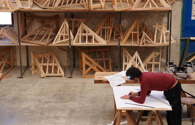 Un apprenti travaille sur son atelier devant une étagère pleine de création en bois